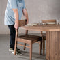 person pushing in a chair at a racetrack oval Maple table 42” wide x 84” long, finished in Coconut W on oval Como pedestal base