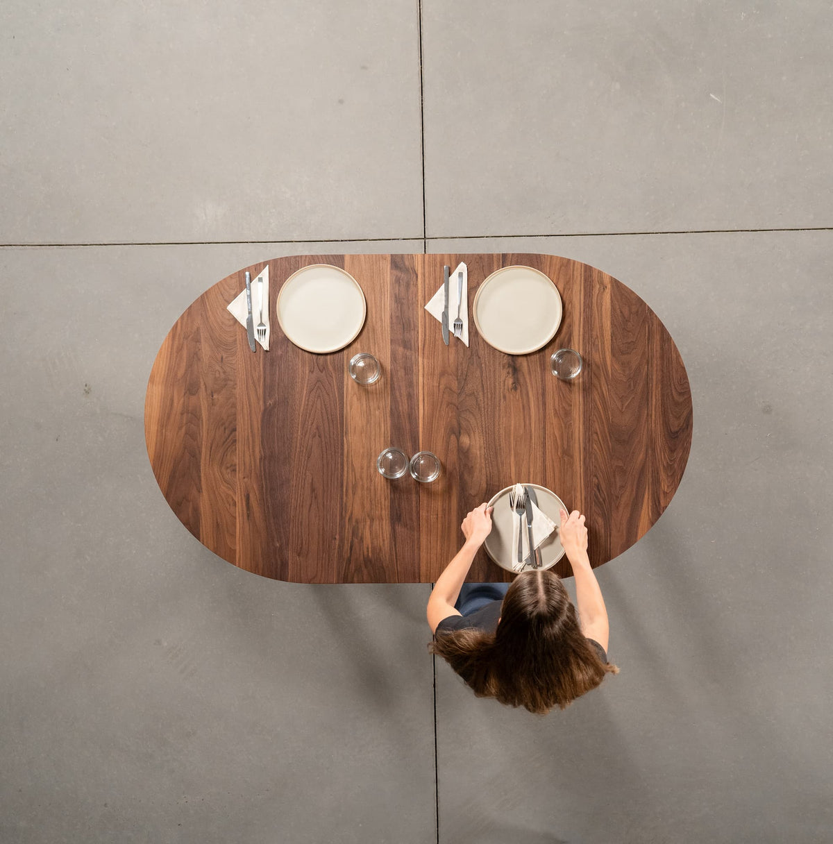 person setting an oval extendable Walnut table 36” wide x 60” long, finished in Pure D