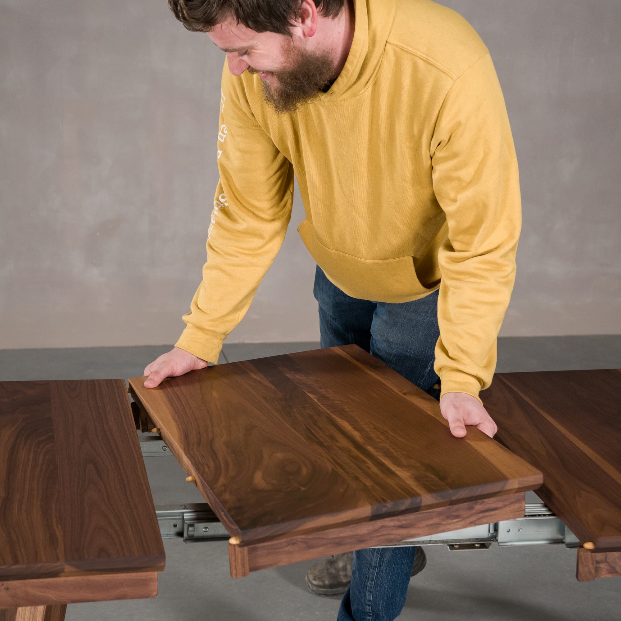 a leaf being added to a square extendable Walnut table finished in Pure D on Caldwell legs 