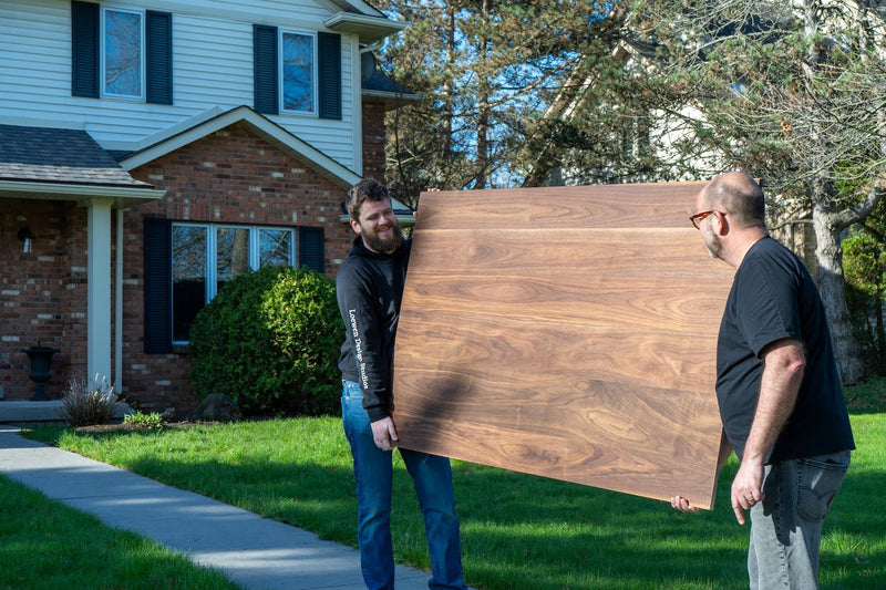 2 men outside carrying a table towards the front door of a home