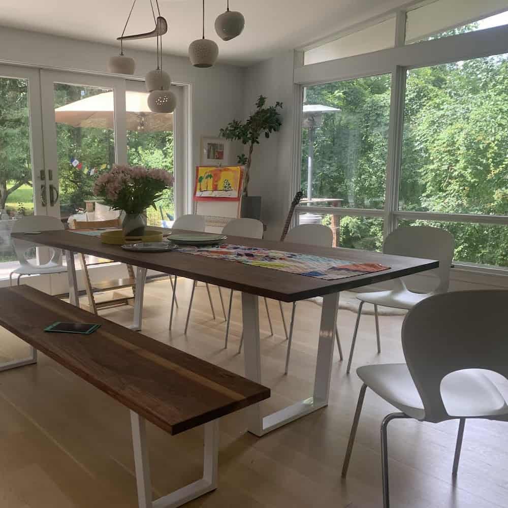Walnut dining table and bench with white steel legs under it with white chairs opposite the bench
